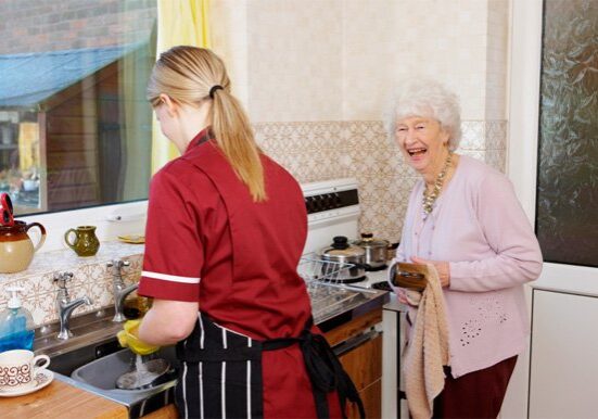 carer helps her elderly pactient by washing the dishes for her